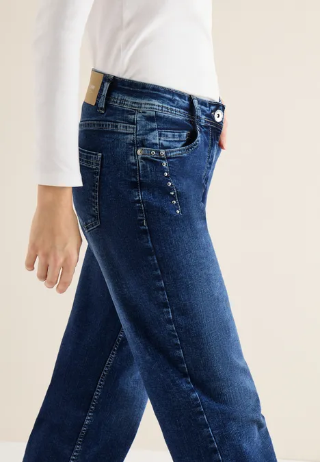 Seitliche Ansicht eines Modells in dunkelblauen Jeans mit dezenten Perlenakzenten an der Tasche.